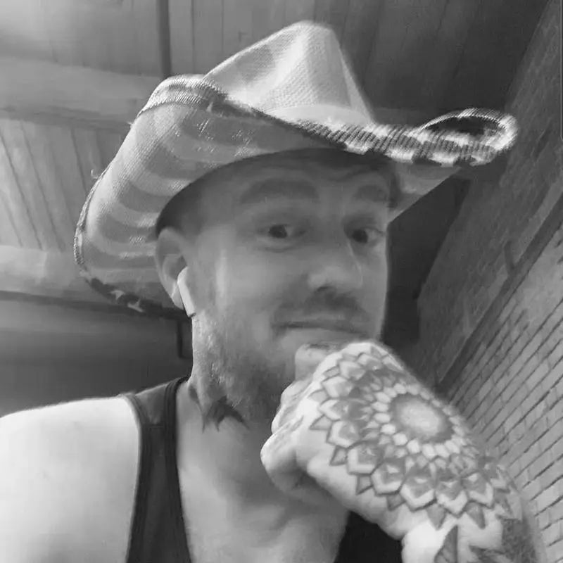 Tattooed man in cowboy hat with mandala hand tattoo, brick wall background, FYT Tattoo Supplies New York