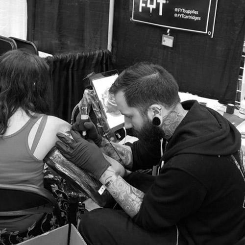 Tattoo artist using FYT tattoo supplies and needle cartridges, tattooing a client's arm in New York studio.