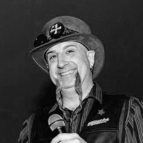 Smiling man with unique beard in steampunk hat holding microphone at event, FYT Tattoo Supplies New York