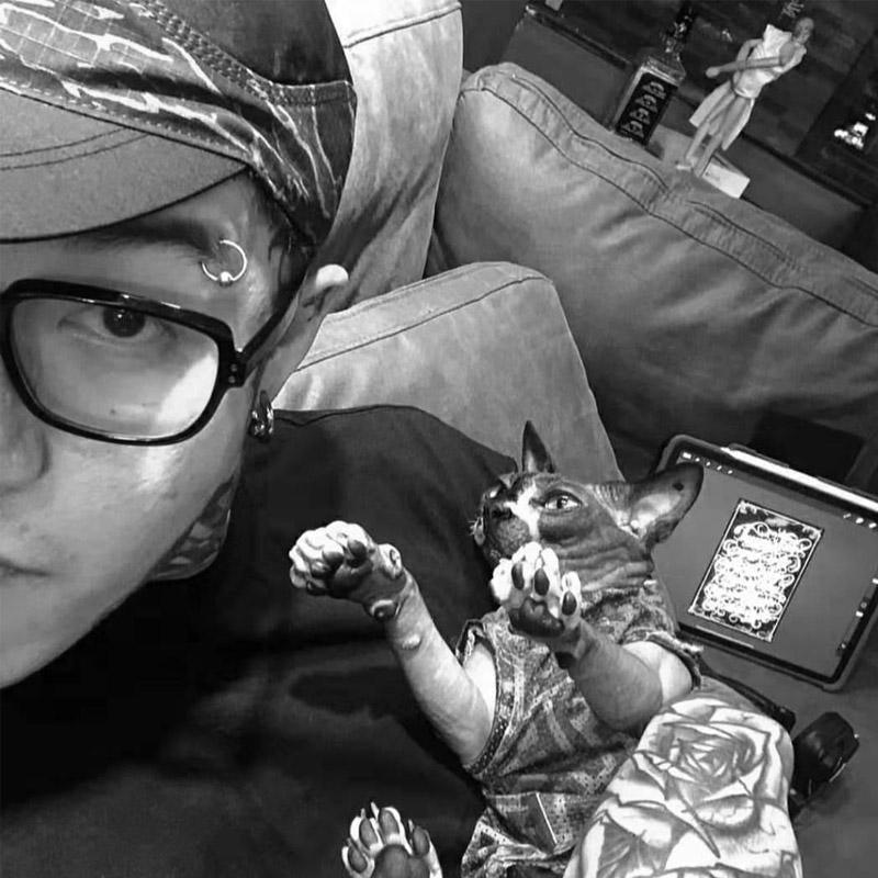 Tattooed artist with glasses and Sphynx cat relaxing on couch, FYT Tattoo Supplies New York